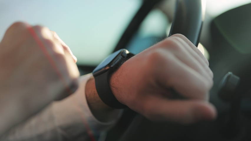 Close-up male hands using modern smart watch in car. Man watch notification. Male hand with a smartwatch holds the steering wheel. Businessman driving car at sunset Royalty-Free Stock Footage #1069718722