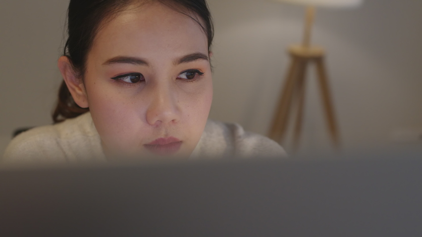 Close up face young asia employee female developer look staring eyes at computer notebook in late night work remotely sit at home office. Business analyst startup project in data financial concept. | Shutterstock HD Video #1069723267