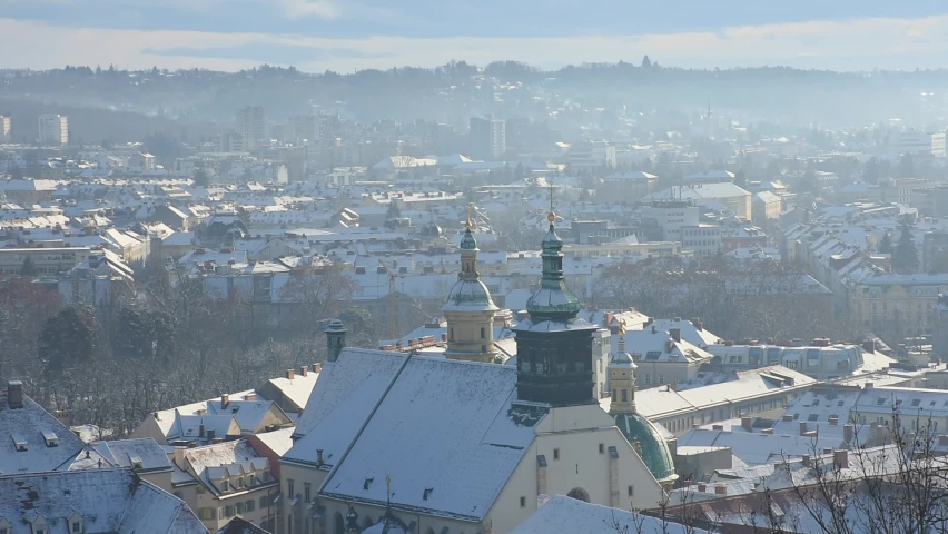Cityscape of Graz with Church of the Sacred Heart of Jesus and historic buildings rooftops with snow in Graz, Styria region, Austria in winter.