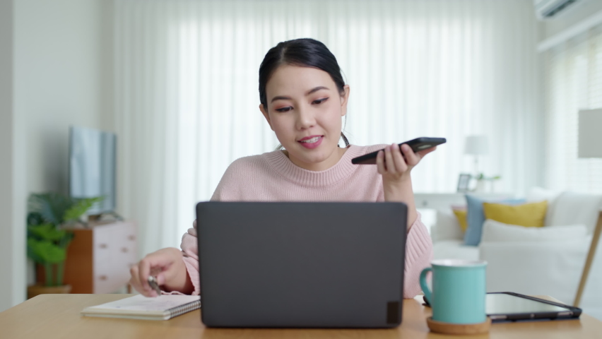 Young happy attractive beautiful asia female staff laugh talk on mobile phone relax comfort sit work on desk table at home. Remotely work on distance job telesale or secretary career for business. | Shutterstock HD Video #1069728340