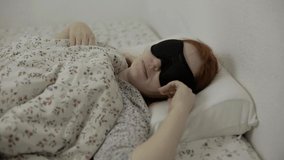 young single woman wakes up in the morning in bed with an eye mask