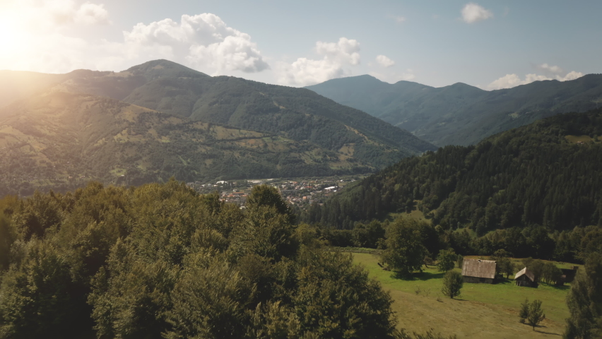 Town in sun mountain valley aerial. Nobody nature landscape. Small cottages at green pine forest. Swiss mounts city. Summer vacation. Rural farmland grass field. Alps countryside, Switzerland, Europe.