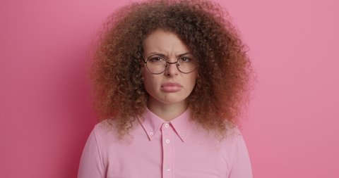 Displeased European teenage girl cannot get rid of acne problem squeezes pimple has puberty period cant deal with blemishes has curly hair wears spectacles and jumper. Problematic skin concept