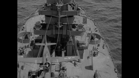 1940s: Looking down on deck of Navy ship with tender on it. Airplane on catapult on deck. Stripped flag waves in wind. Looking down on deck of ship with airplane on catapult.