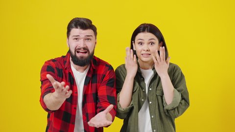 Portrait of shocked couple against yellow background. Boy and girl look surprisingly at camera, hear bad news, express their reaction