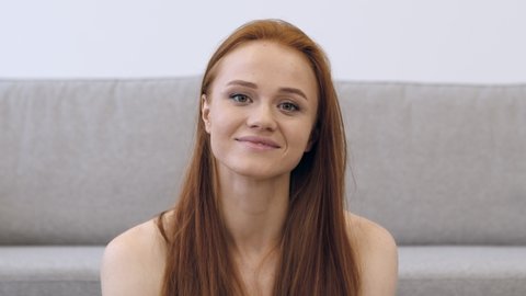 Attractive Red-Haired Young Woman Posing Shirtless Playing With Beautiful Hair And Flirting Looking At Camera Playfully Sitting Near Couch At Home. Female Beauty And Sensuality Concept