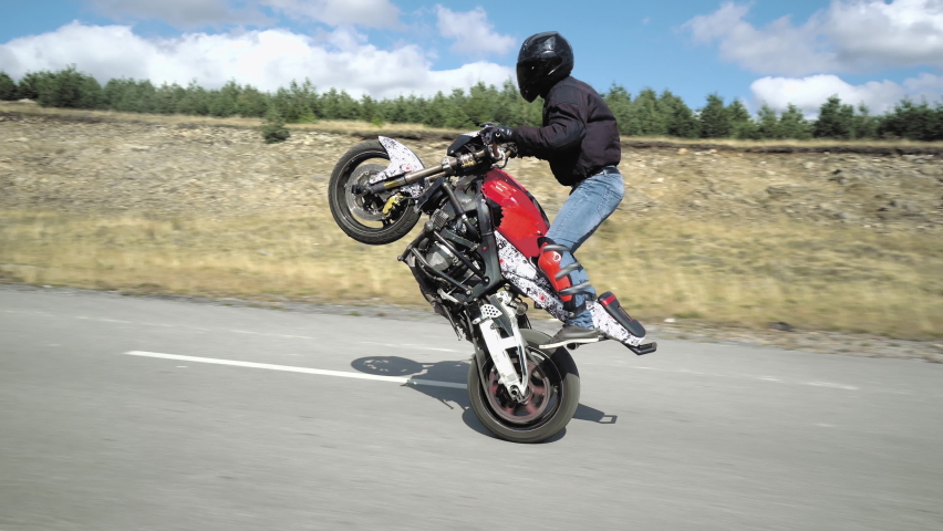 Biker man making a stunt, driving the motor cycle on the back wheel only, extreme driving | Shutterstock HD Video #1069739401