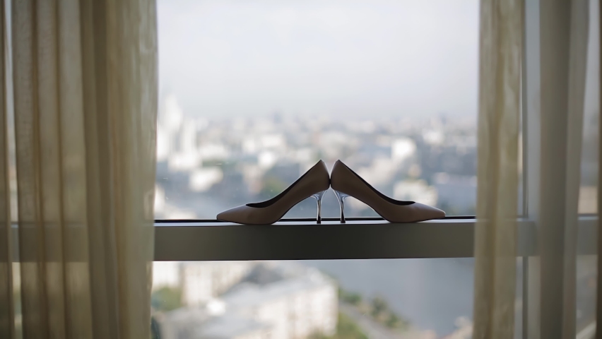 Women's shoes stand on the window and in the background you can see the big city and the sky. Cool stylish shots