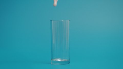 Super Slow Motion of Pouring Milk in Transparent Glass, Blue Background 