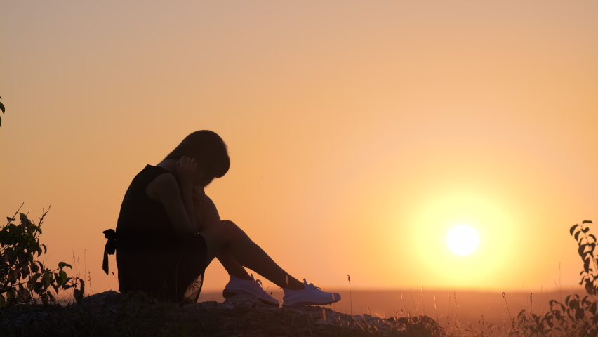 Young elegant woman in black short dress and white sneaker shoes sitting on a rock relaxing outdoors at summer evening. Fashionable lady enjoying warm sunset in nature.