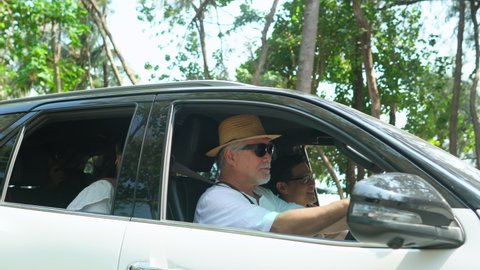 Happy Asian family in car having fun together with outdoor lifestyle activity on summer beach road trip vacation. Healthy senior man driving car with talking and looking to beautiful beach with family