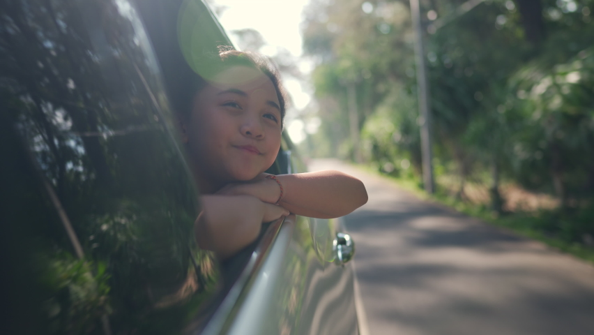 Happy Asian family enjoy and fun travel together and outdoor lifestyle activity on road trip vacation. Little child girl kid sit in the car with pull her face and hand out of car window in summer day