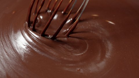 Chocolatier make organic bitter hand-crafted chocolate dessert with nuts. Candy making, confectionery concept. Slow motion mixing, stirring premium dark melted liquid chocolate with a whisk in a bowl