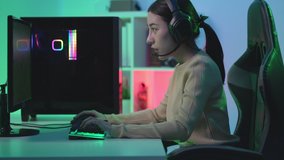Asian girl gamer in headset playing and winning in online video game with green chroma key screen computer in colorful neon lights room at home