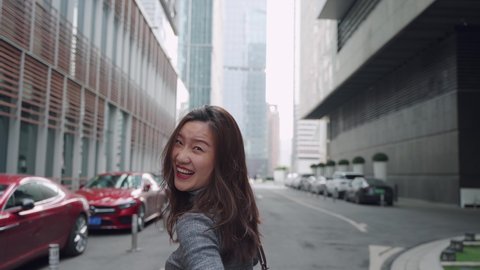 4K slow motion beautiful Asian girl running on the city street, looking back and smiling at the camera Chinese girl running in the Chengdu city center surrounded by tall office buildings