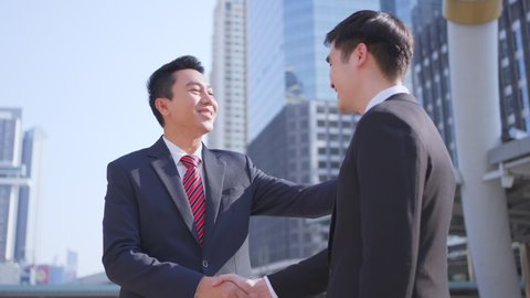 Asian businessman making handshake in the city building in the background. A partnership agreement is successful after complete the negotiation. Business deal, merger and acquisition concepts.