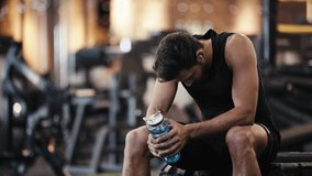bearded sportsman listening music and drinking water in gym