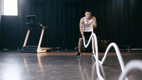 Slow-motion of sportive man exercising with battle ropes