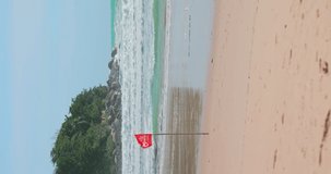 Vertical video. Red flag alert. Beach is danger for swimming. Red flag fluttering to alert people not to swim because of strong storm wind and waves. Sunny beach with huge blue waves. Lifeguard.