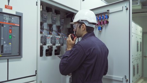 An engineer man or worker, people using a tablet device, working in electrical room. Power energy motor machinery cabinets in control or server room, operator station network in industry factory.
