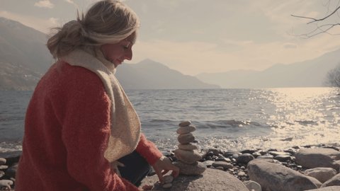 Woman stacking rocks by the lake, relaxing moment 