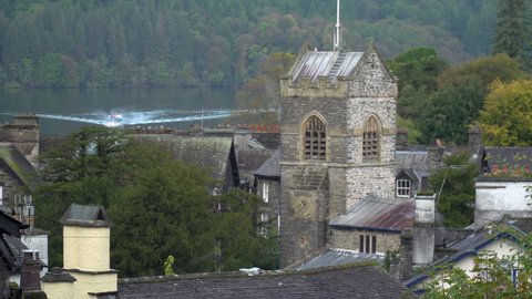 View across Bowness-on-Windermere with lake and church. Village rooftops in scenic English Lake District. Popular holiday and tourist destination in scenic mountain area. Small towns for visitors.