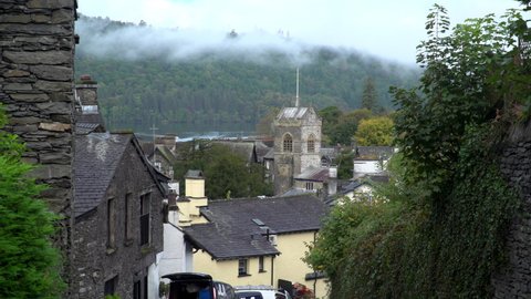 View across Bowness-on-Windermere in England. Lake District. With lake, church and forest. Wide shot with homes and rooftops, forest and asmotpheric low cloud. Popular holiday destination 