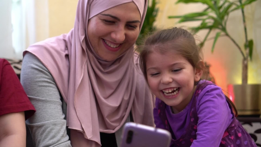Ramadan Celebrations Online. Happy traditional Muslim family, mother in hijab and children together at home using smartphone to call friends during quarantine. Eid mubarak