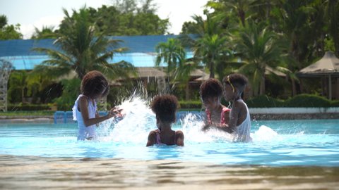 group of happy african american kid having fun playing and splashing in swimming pool together at water park outdoors in summer holidays