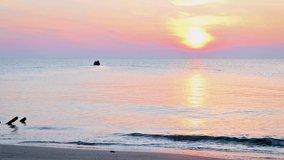 Video with colorful close up view of a sandy beach at sunrise and a small fishing boat in the distance. Dramatic sea sunrise, tender pink sky and shining waves.