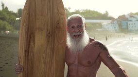 Fitness senior having fun surfing at sunset time - Sporty bearded man training with surfboard on the beach - Elderly healthy people lifestyle and extreme sport concept - Powered by Shutterstock - Get 15% off with code: PIKWIZARD15