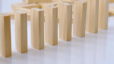 Domino effect, row of wooden domino falling down on white background. Dominoes falling in a row, hand pushes a Domino and starts a chain reaction Board game. Falling dominoes