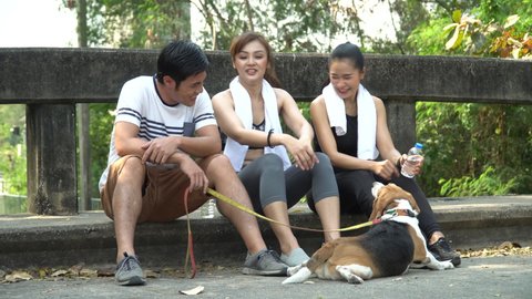 group of fitness asian people  wearing sportswear and towel  take a break after workout sitting on road playing with dog in park outdoors . friend with dog 