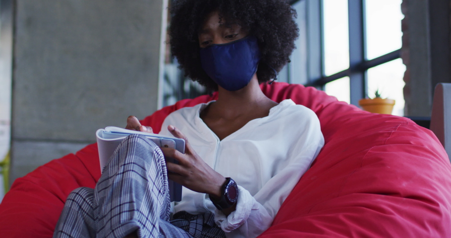 African american woman wearing face mask sitting in cafe writing in notebook. digital nomad on the go during coronavirus covid 19 pandemic. | Shutterstock HD Video #1069783165