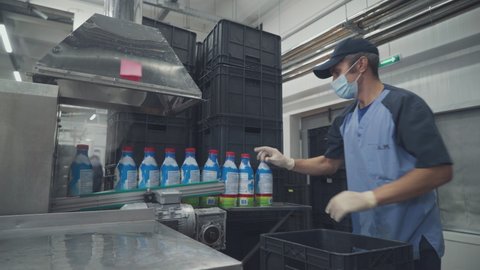 A Male Worker Takes And Stacks Milk Bottles Moving On The Conveyor. Dairy Food Production Line. Automated Process. Manual Labor. Plastic Packaging. Modern Machine. Inside A Manufacturing Facility.