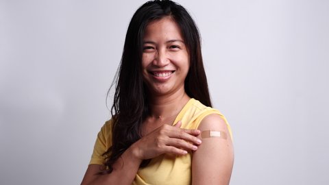 Woman wearing medical face mask showing her arm after getting vaccinated with feeling happy. Concept of vaccination, vaccinated patient, vaccine roll-out program, Coronavirus, COVID 19.