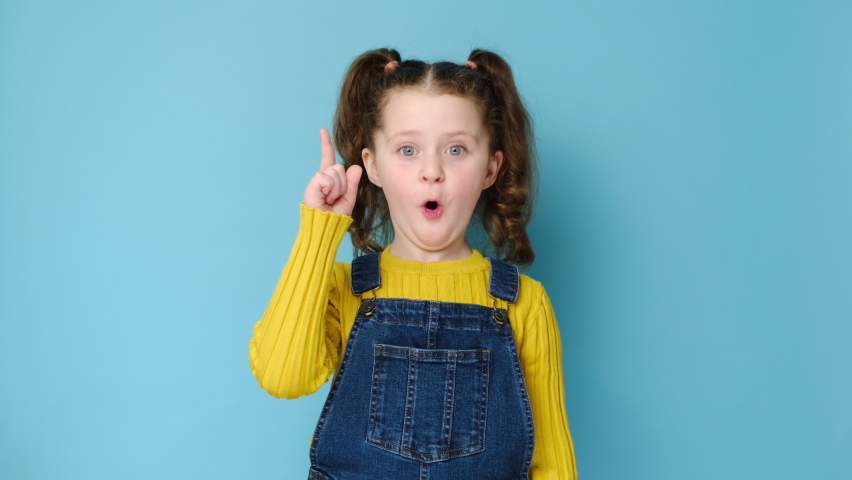 Portrait of funny little preschool girl make gesture raises finger came up with creative plan feels excited with good idea, inspiration motivation, isolated on blue background. Work eureka concept | Shutterstock HD Video #1069791628