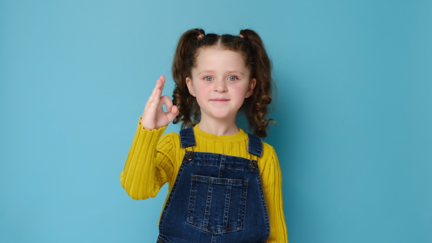 Portrait of beautiful caucasian little girl showing okay gesture, looking at camera with friendly smile, isolated on blue studio background with copy space. Agreement, approval, confirm, ok concept | Shutterstock HD Video #1069792708