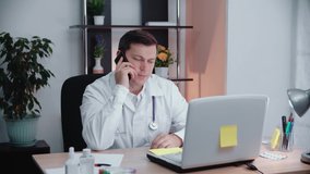 Male doctor sitting in the office in his office talking on the phone.