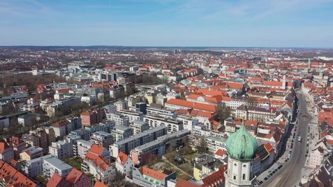 St Ulrich u. Afra Church. Augsburg city center. Church in Augsburg. Drone flying at low above buildings with red tiled roof moving opposite cathedral dome and clock tower.
