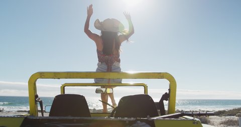 Happy caucasian woman sitting on beach buggy by the sea waving hands. beach stop off on summer holiday road trip.