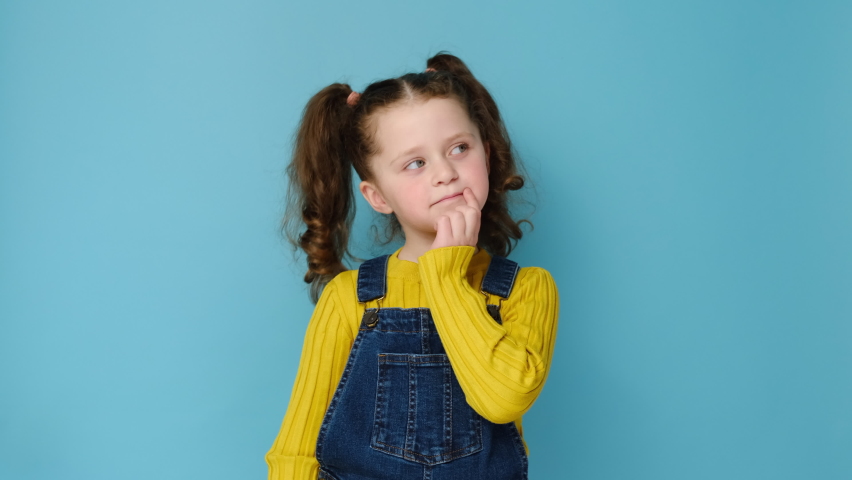 Portrait of thoughtful little girl child touch chin with finger thinking or considering, pensive lovely small kid making decision imagining idea, isolated over blue studio background with copy space | Shutterstock HD Video #1069795045