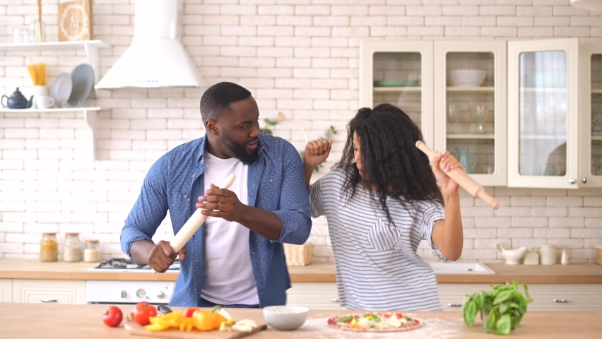 Happy joyful black couple husband and wife having fun singing in the kitchen, cooking together at home. Overjoyed young couple in love preparing meal healthy food, enjoying active family weekend Royalty-Free Stock Footage #1069795270