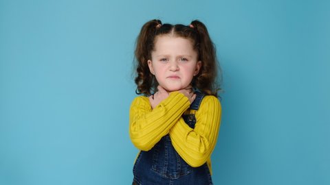 Unhealthy little girl child touch neck feels discomfort painful feelings hard to swallow, sore throat pain irritation or loss of voice, models over blue studio background. Tonsillitis angina concept