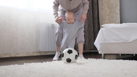 Mother and little child, son play football in room, kick soccer ball. Kid, infant, enjoys playing with his mother at home. Happy, Healthy, sporty family. Develop your child through active sports games