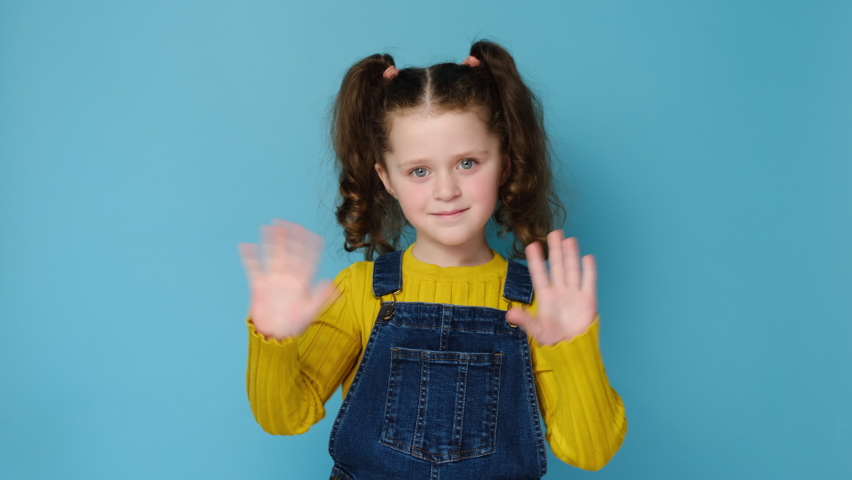 Attractive beautiful joyful cute little caucasian girl child point finger camera on you waving meeting greeting with hands as notices someone, isolated over blue studio background wall. Hello concept | Shutterstock HD Video #1069795729