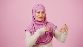 Inspired middle aged muslim woman dancing traditional dance and smiling to camera over pink background