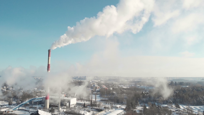 Aerial drone shot of white steam out of heat plant chimneys pipes during cold day in winter with city in the background seen through the smoke. Clear blue sky sunny weather. Flying up ascending | Shutterstock HD Video #1069796638