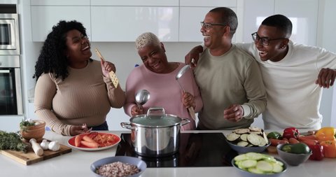 Happy black family having fun cooking and dancing together inside kitchen at home 