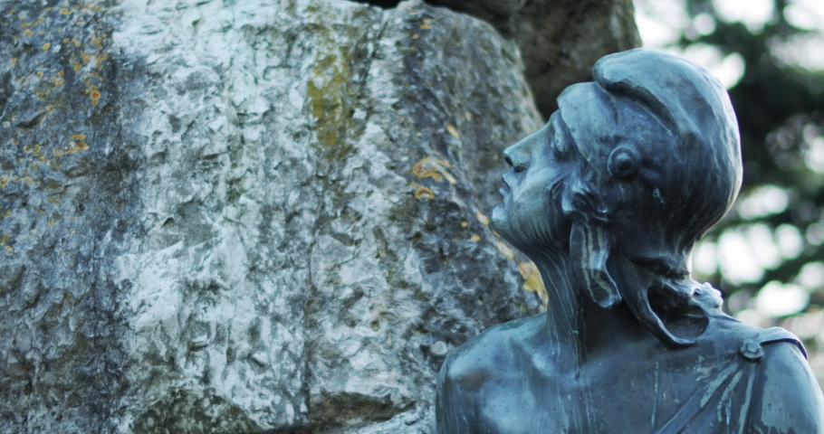Black sculpture of a young lady made of stone in a city park. Slow motion, close up.
